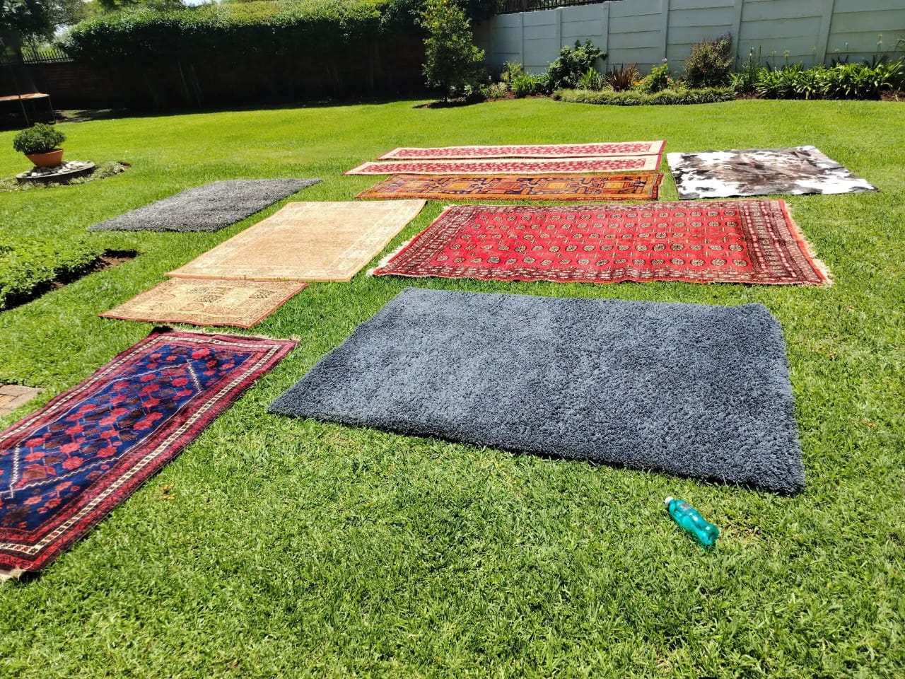 A collection of patterned and plain rugs laid out on a lawn during an Estlas job